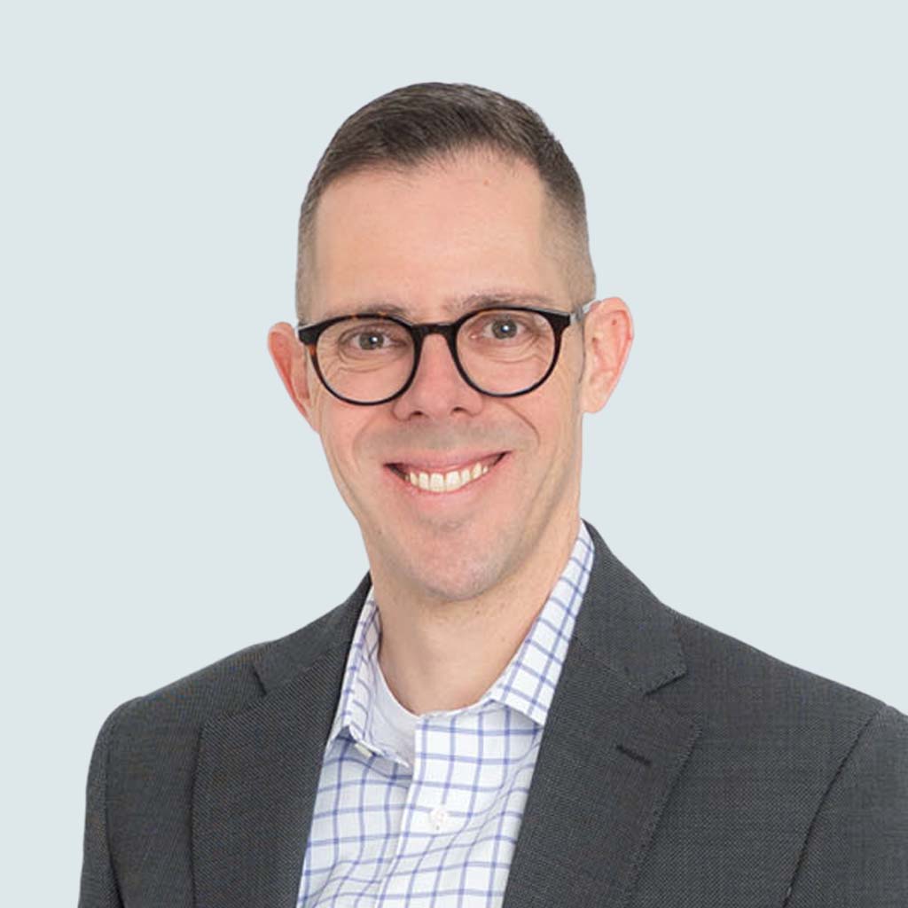 Roger Heid, Founding Partner of Transatlantic Search, in a professional executive headshot wearing a dark blazer and checkered shirt, photographed against a light grey background.